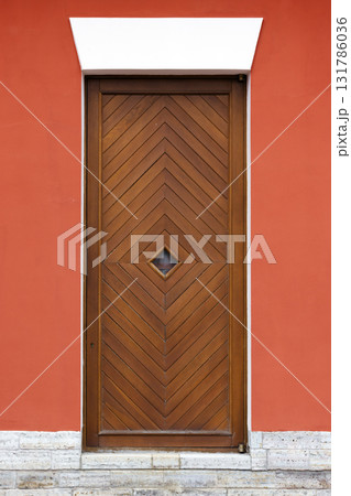 A tall wooden door featuring a chevron pattern sits within a vivid red wall 131786036
