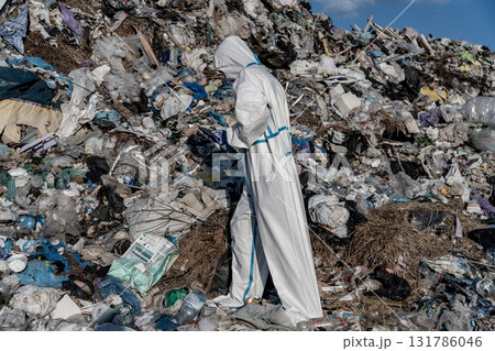 A person dressed in protective clothing examines the extensive garbage at a landfill, highlighting the serious issue of pollution A person dressed in protective clothing examines the extensive garbage at a landfill, highlighting the serious issue of pollution 131786046