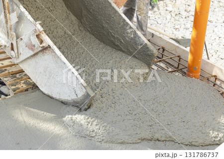 Pouring fresh ready-mixed concrete from wheelbarrow on floor during for construction of a house 131786737