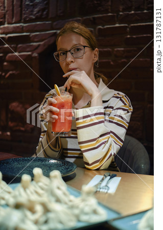 Young woman enjoying a refreshing drink at a cozy restaurant with elegant decor 131787131
