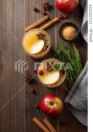 Two glasses of hot apple cider with cinnamon, anise, brown sugar and rosemary on a wooden background Two glasses of hot apple cider with cinnamon, anise, brown sugar and rosemary on a wooden background 131787354