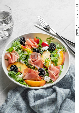 Fresh salad with peaches, arugula, feta, prosciutto and berries in a plate on a light background Fresh salad with peaches, arugula, feta, prosciutto and berries in a plate on a light background 131787513