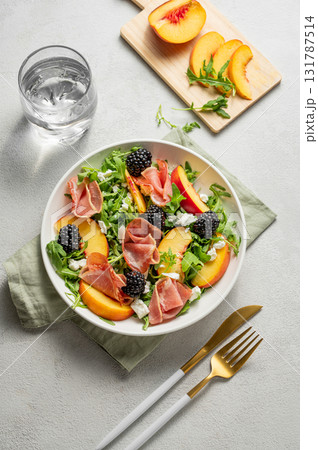 Fresh salad with peaches, arugula, feta, prosciutto and berries in a plate on a light background Fresh salad with peaches, arugula, feta, prosciutto and berries in a plate on a light background 131787514