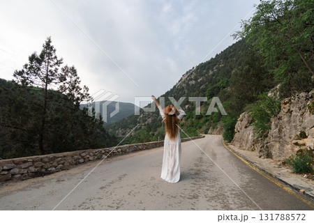 A woman in a white dress is standing on a road, waving her hand 131788572