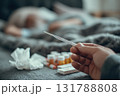 Hand Holding Thermometer with Sick Person in Bed and Medicine Nearby 131788808