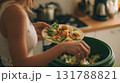 Woman Disposing Salad into Green-Lined Trash Bin in Modern Kitchen 131788821
