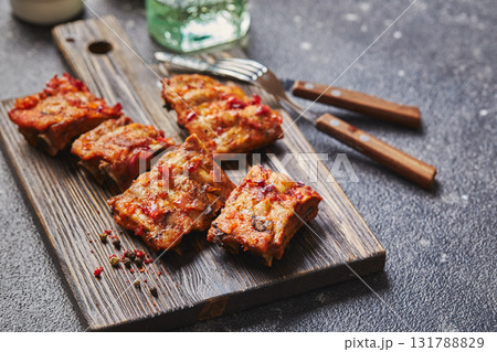 Grilled baked pork ribs with spices on wooden cutting board on dark background. American food concept. Grilled baked pork ribs with spices on wooden cutting board on dark background. American food concept. 131788829