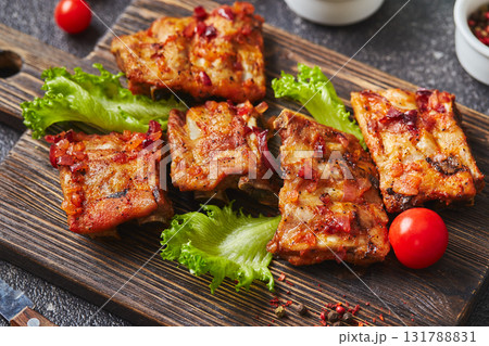 Grilled baked pork ribs with spices and vegetables on wooden cutting board on dark background. American food concept. 131788831