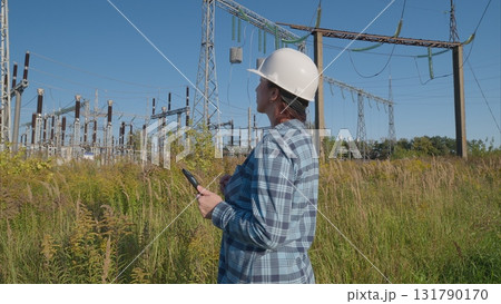 A worker in safety gear at an electrical substation ensures safety and compliance A worker in safety gear at an electrical substation ensures safety and compliance 131790170