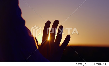 Silhouette of a Hand Against a Beautiful Sunset with a Glowing Light in the Background Silhouette of a Hand Against a Beautiful Sunset with a Glowing Light in the Background 131790241