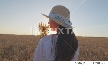 A Serene Woman Strolling Through a Wheat Field at Sunset Surrounded by Beautiful Flowers 131790327