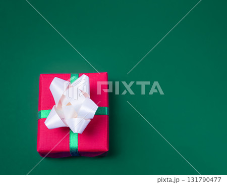 Christmas gift in a red box with white bows on a green background, with empty space for text 131790477