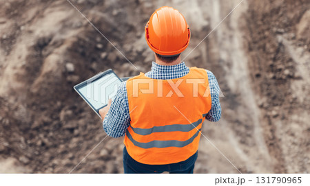 Construction worker using tablet on site, wearing safety gear and helmet 131790965