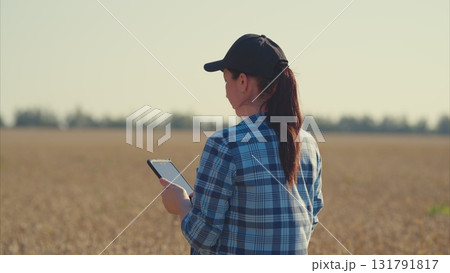 A Young Woman Actively Engaged in Using a Tablet While Standing in a Beautiful Field A Young Woman Actively Engaged in Using a Tablet While Standing in a Beautiful Field 131791817