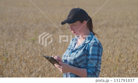 A woman is seen utilizing a tablet in a vast wheat field on a bright and sunny day 131791837