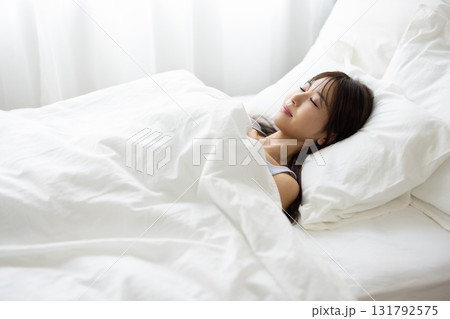 朝の光に包まれて白いベッドで眠る女性 朝の光に包まれて白いベッドで眠る女性 131792575