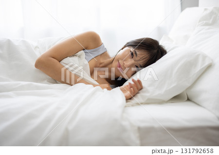 朝の光に包まれて白いベッドで微笑む若い女性 朝の光に包まれて白いベッドで微笑む若い女性 131792658
