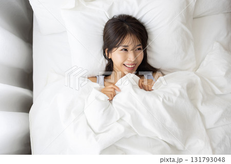 朝の光に包まれて白いベッドで微笑む若い女性 朝の光に包まれて白いベッドで微笑む若い女性 131793048