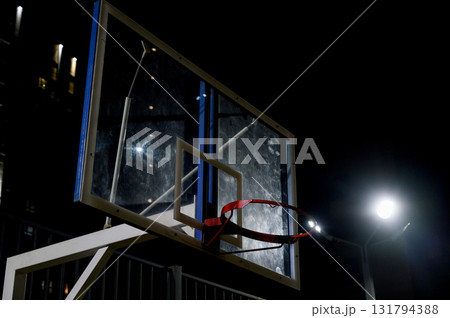Close-up of a basketball backboard and red ring at night. 131794388