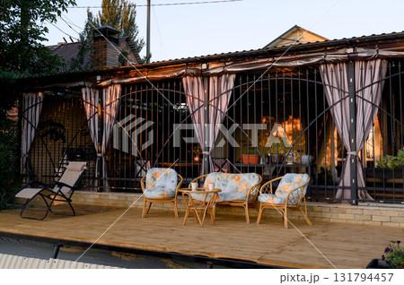 A seating area with rattan chairs and a table on the house's open wooden deck. 131794457