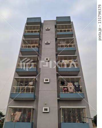 Low angle view of a tall, narrow apartment building with multiple balconies and windows against a cloudy sky 131796376