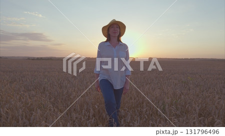 Enjoying a delightful sunset stroll amidst the vast golden fields while wearing a stylish farm hat Enjoying a delightful sunset stroll amidst the vast golden fields while wearing a stylish farm hat 131796496