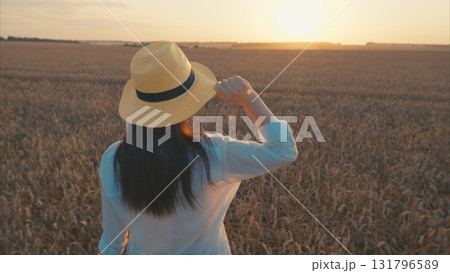 A graceful woman quietly observes the stunning sunset draping over an endless golden wheat field A graceful woman quietly observes the stunning sunset draping over an endless golden wheat field 131796589