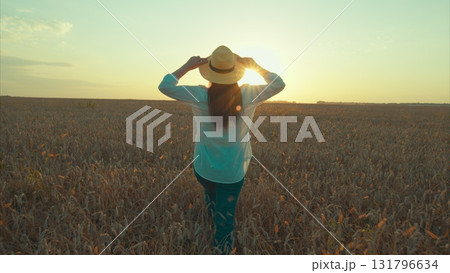 A Woman Enjoys a Leisurely Stroll Through a Golden Wheat Field Beneath a Stunning Sunset Sky 131796634