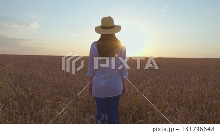 A woman wearing a hat is Walking peacefully while watching the beautiful sunrise over a vast field 131796648