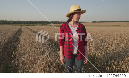 A woman stands in a beautiful wheat field, elegantly wearing a straw hat, enjoying the scenery 131796660