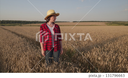 A Woman Standing in a Wheat Field, Elegantly Wearing a Straw Hat Under the Bright Sun 131796663