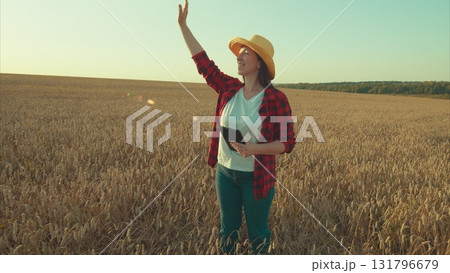 A Woman is immersed in a Wheat Field, equipped with her Tablet and wearing a Straw Hat 131796679
