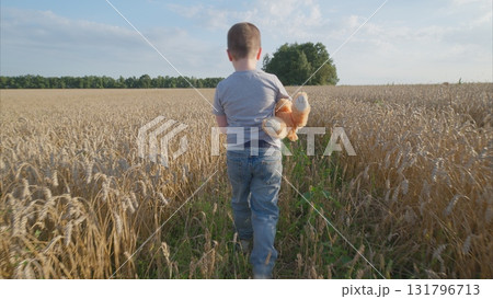 A child joyfully exploring a vast golden wheat field while holding a toy in hand 131796713