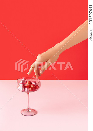 Beautiful well-groomed female hand with pink matte nails and heart-shaped candies on a pink background. Valentines Day concept 131797041
