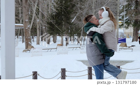Romantic couple embracing, male partner lifting female partner amid snow covered park landscape, sharing intimate winter moment together Romantic couple embracing, male partner lifting female partner amid snow covered park landscape, sharing intimate winter moment together 131797180