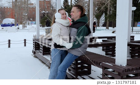 Loving couple cuddling on park bench during winter, sharing tender moment amid snowy landscape, affectionately looking into each other's eyes 131797181