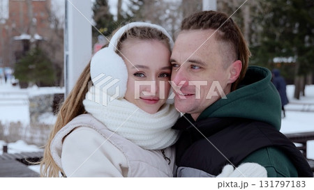 Young couple bundled in winter attire, embracing warmly and savoring a romantic moment in a picturesque snowy park, surrounded by trees and the beauty of wintertime Young couple bundled in winter attire, embracing warmly and savoring a romantic moment in a picturesque snowy park, surrounded by trees and the beauty of wintertime 131797183