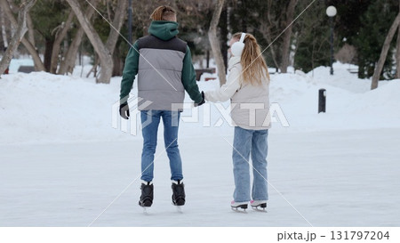 Young couple enjoys a romantic day out, holding hands while ice skating in a snowy winter park, creating a heartwarming scene of togetherness and leisure Young couple enjoys a romantic day out, holding hands while ice skating in a snowy winter park, creating a heartwarming scene of togetherness and leisure 131797204