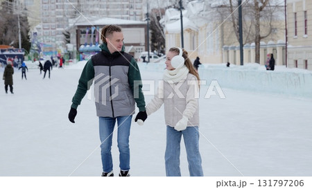 Cheerful couple gliding hand in hand across frosty outdoor skating rink, sharing joyful winter moment in urban landscape 131797206