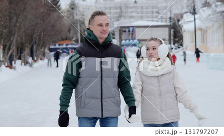 Cheerful couple walking hand in hand on snow covered ice rink, sharing warm embrace amid winter holiday celebration and festive surroundings 131797207