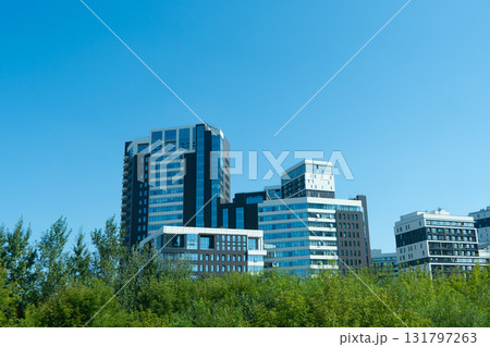 Modern Architectural Designs of High-Rise Buildings Surrounded by Lush Greenery Against a Clear Blue Sky Modern Architectural Designs of High-Rise Buildings Surrounded by Lush Greenery Against a Clear Blue Sky 131797263