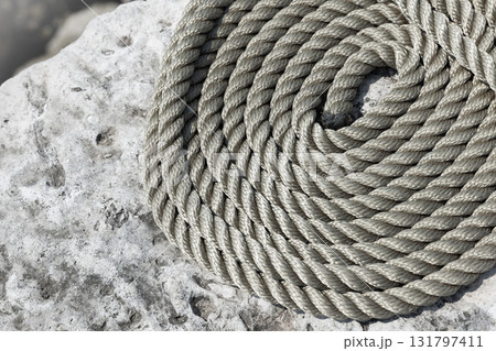 A thick, gray rope neatly coiled on a weathered rock surface 131797411