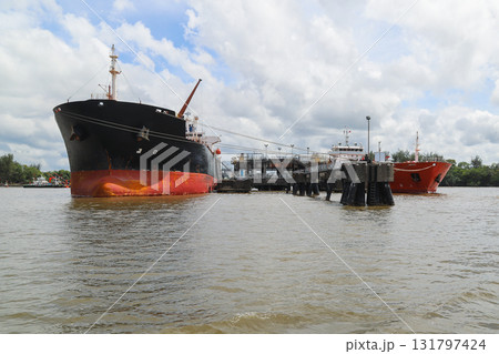 A large black tanker ship with a red hull sits anchored at a weathered oil jetty 131797424