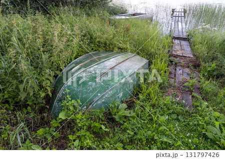 An abandoned green boat lies upside downin tall grasses on the lake coast 131797426