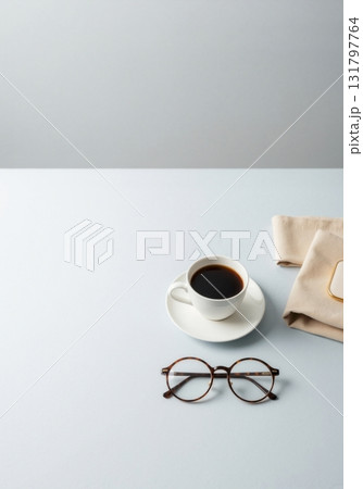 A cup of coffee and eyeglasses on a minimalist blue desk. Modern office workspace or study concept with copy space. A cup of coffee and eyeglasses on a minimalist blue desk. Modern office workspace or study concept with copy space. 131797764