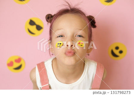 Funny girl with smiley icons pasted on her face and pink studio background. World Social Media Day. Using emoji to convey emotions in messages and social networks. 131798273