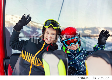 Portrait of two happy kid boys enjoy having fun sit ski lift gondola at alpine mountain skiing resort on bright winter day. Teen beginner skier rest of training in ski school Portrait of two happy kid boys enjoy having fun sit ski lift gondola at alpine mountain skiing resort on bright winter day. Teen beginner skier rest of training in ski school 131798282