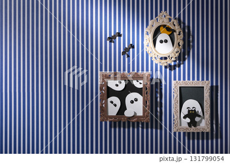 Handmade Halloween wall decorations: paper portraits of ghosts and bats in frames against a blue and white striped background. Space for your text. Handmade Halloween wall decorations: paper portraits of ghosts and bats in frames against a blue and white striped background. Space for your text. 131799054