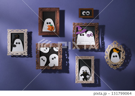 Handmade paper crafts for Halloween. Purple wall with portraits of ghosts with pumpkins, cats, and bats. Paper art. Handmade paper crafts for Halloween. Purple wall with portraits of ghosts with pumpkins, cats, and bats. Paper art. 131799064
