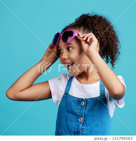 Happy, smile and of a child with sunglasses in studio with positive, energy and excited face expression. Happiness, childhood and girl kid model with funky, trendy and cool glasses by blue background 131799563